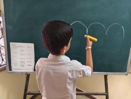 Young student practicing writing patterns on classroom chalkboard